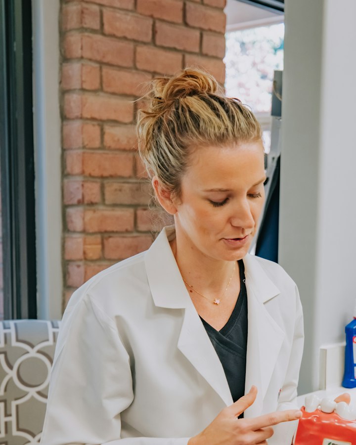 Dr Eleanor Marsh in a white clinical coat, pointing to a tooth on a dental model.